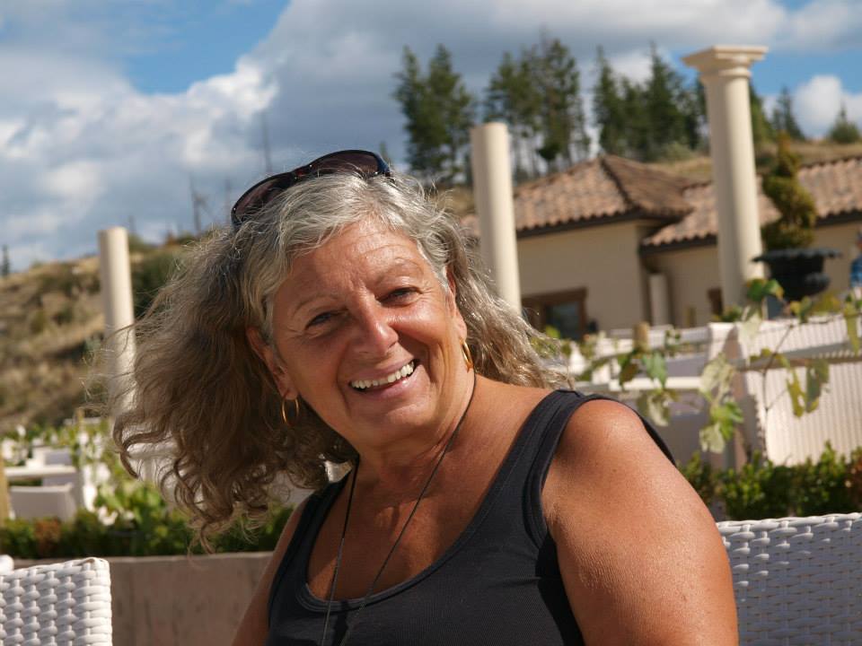 Portrait of a smiling woman with long grey hair in a black shirt and glasses on her head.