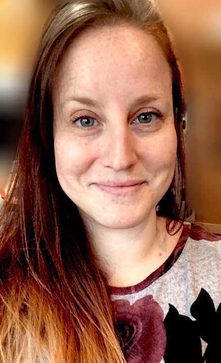 Portrait of a smiling woman with long reddish-brown hair in a flowered shirt.