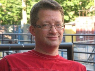 Portrait of a smiling man wearing glasses with brown hair and a red shirt