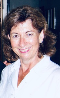 Portrait of a smiling woman with wavy brown hair and a white shirt.