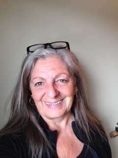 Portrait of a smiling woman with long grey hair in a black shirt and glasses on her head.