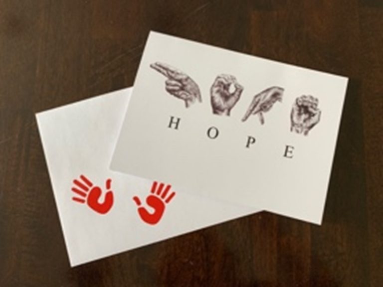 A greeting card on top of an envelope with two red open hand imprints in the bottom left corner. Horizontally across the center of the card are the sketched ASL letters to spell ‘HOPE’. Below the sketched hands are the corresponding individual letters.