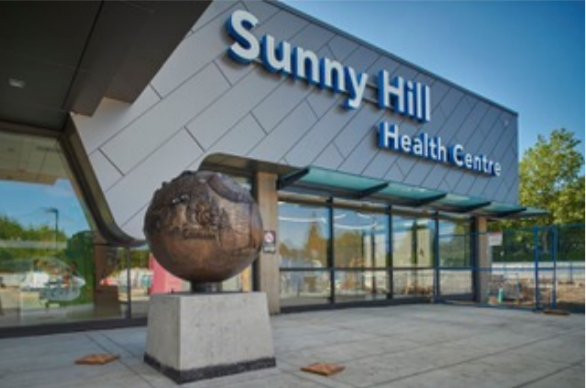Photo of the front of a brown building with many windows. Sunny Hill Health Centre is on the building in large white letters.